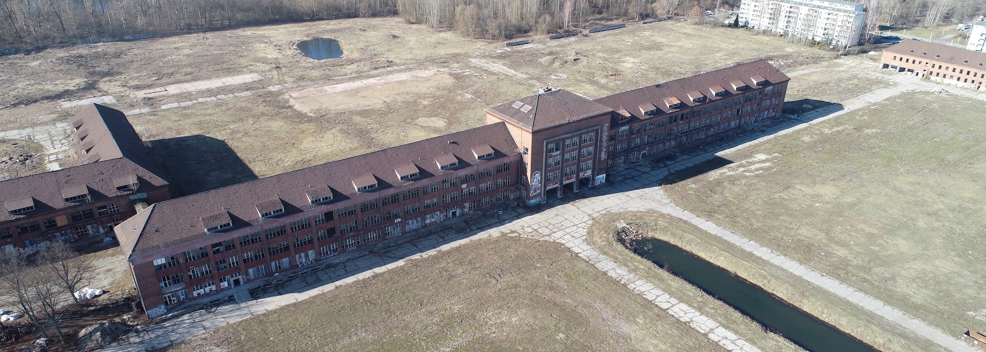 Luftaufnahme eines langen, roten Backsteingebäudes mit Wiese.