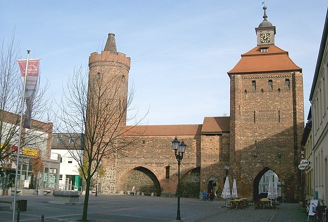 Historisches Stadttor mit Türmen und Platz im Vordergrund.