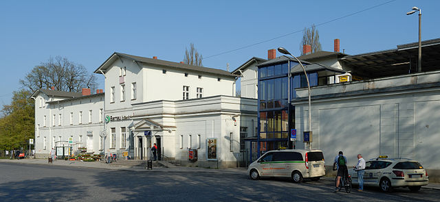 Bahnhof mit geparkten Autos und Personen im Vordergrund.